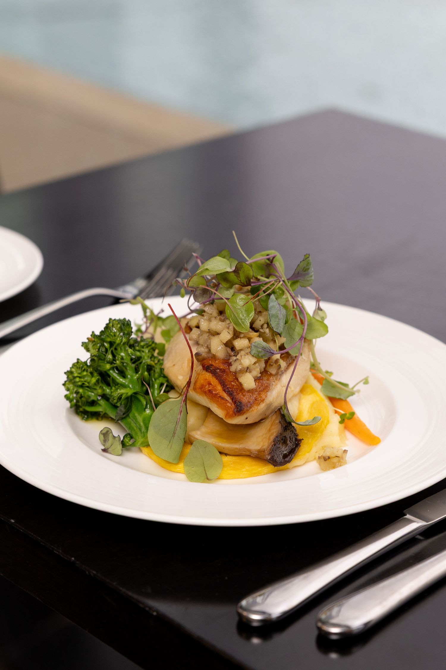 Elegantly plated fine dining dish with microgreens and sauce on white plate against dark background.