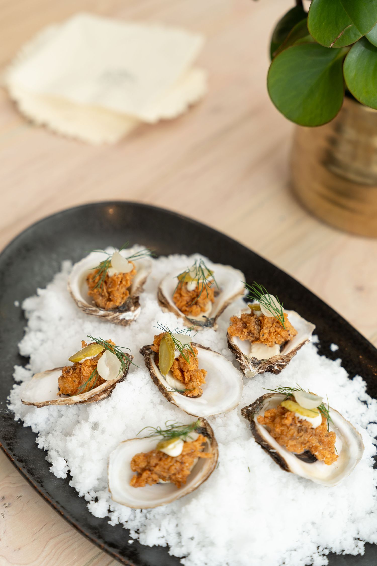 Fresh oysters on ice garnished with orange toppings and herbs on a black serving platter.