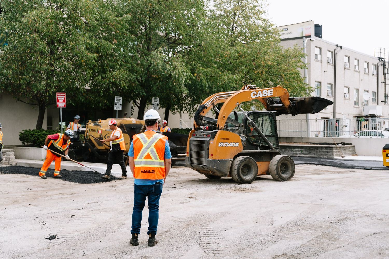 Construction workers in safety gear inspect road paving equipment and machinery on a job site.