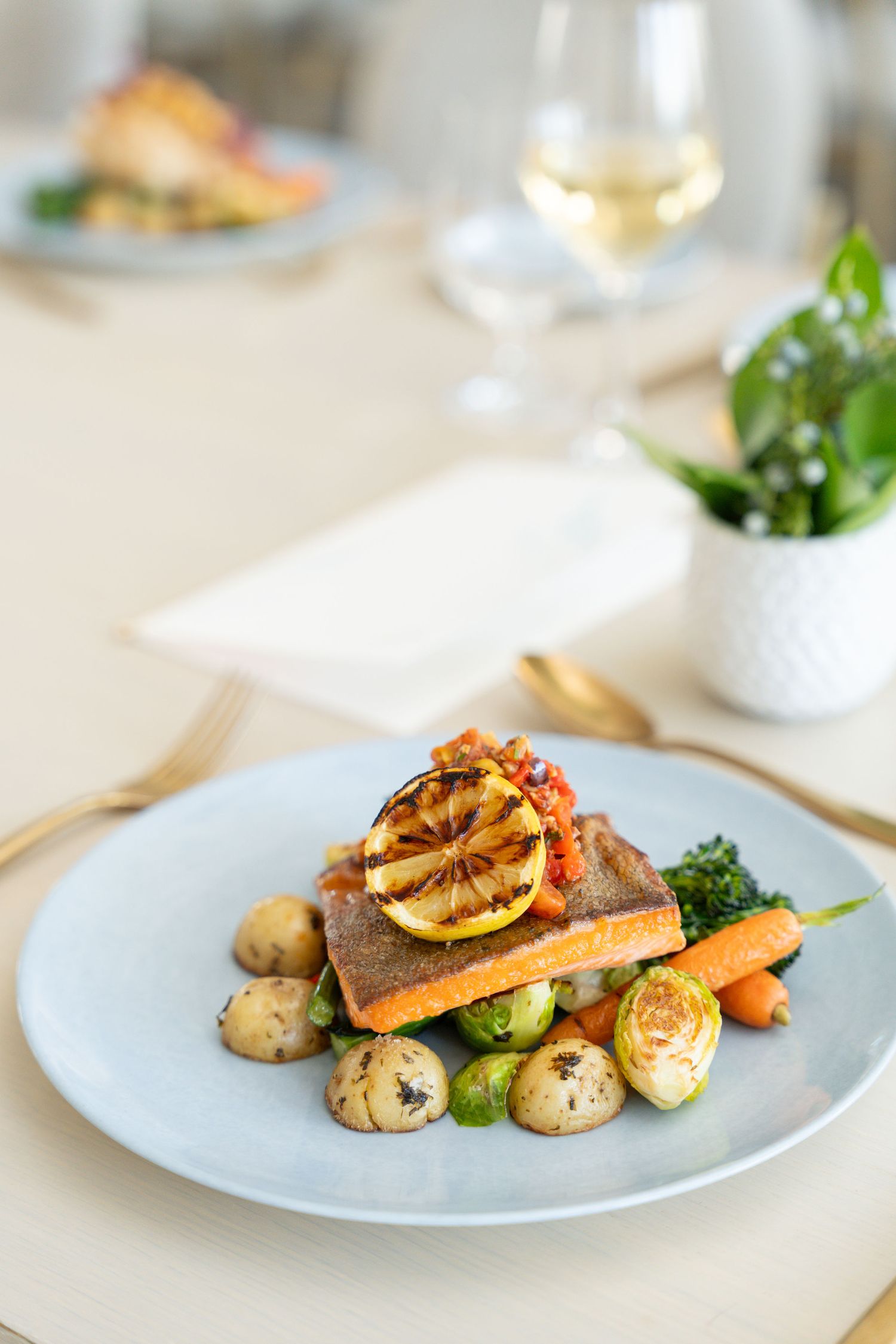 Elegant plated salmon dish with roasted vegetables and citrus garnish served on white plates in a fine dining setting.