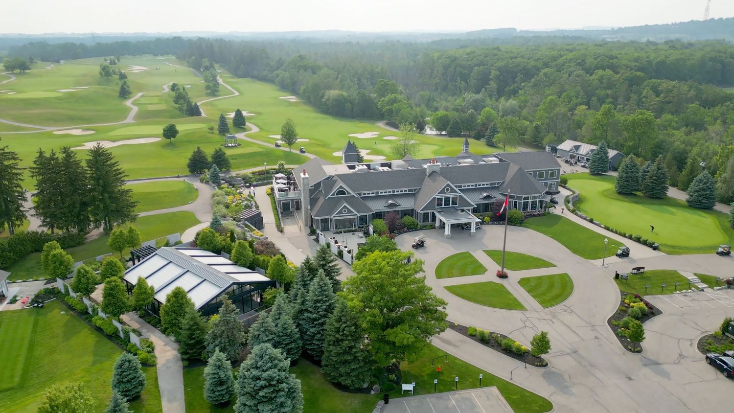 Aerial panoramic view of a golf resort with rolling green fairways, trees, and clubhouse buildings nestled in lush landscape.