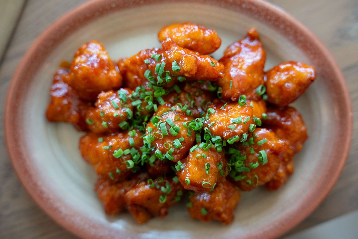 Sweet and spicy Korean-style chicken pieces garnished with fresh herbs on a rustic ceramic plate.