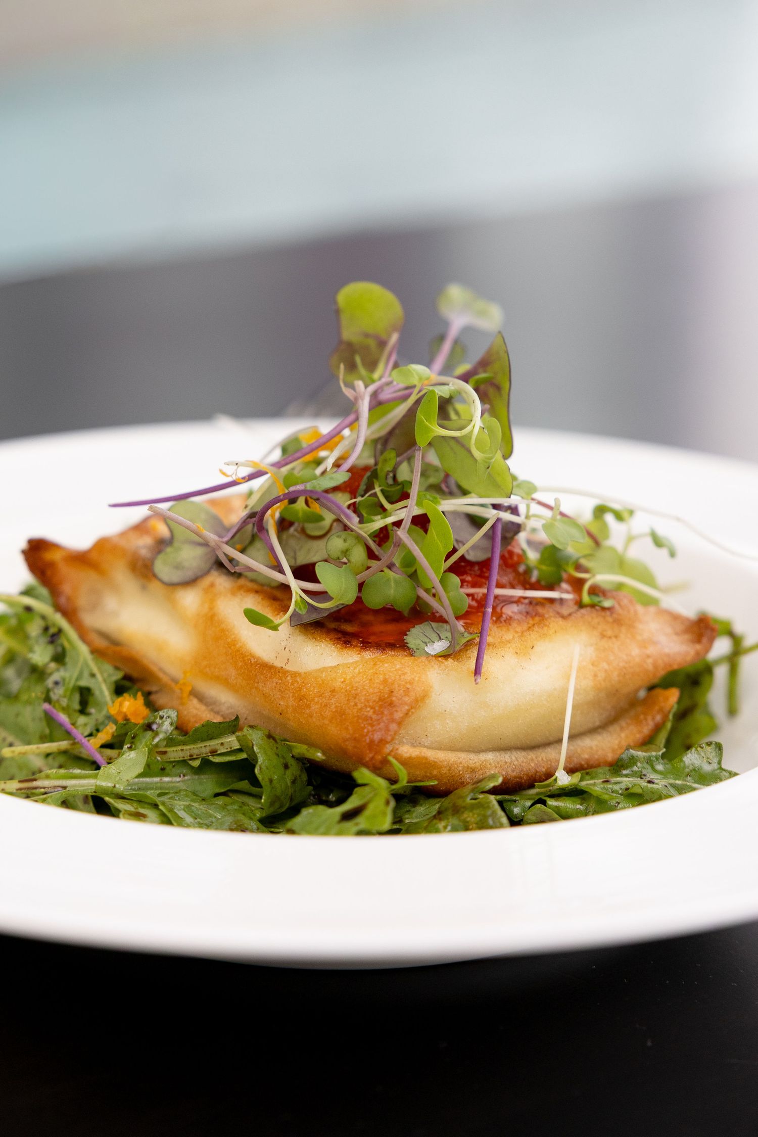 Elegantly plated fish dish garnished with fresh microgreens and served on a white plate against dark background.
