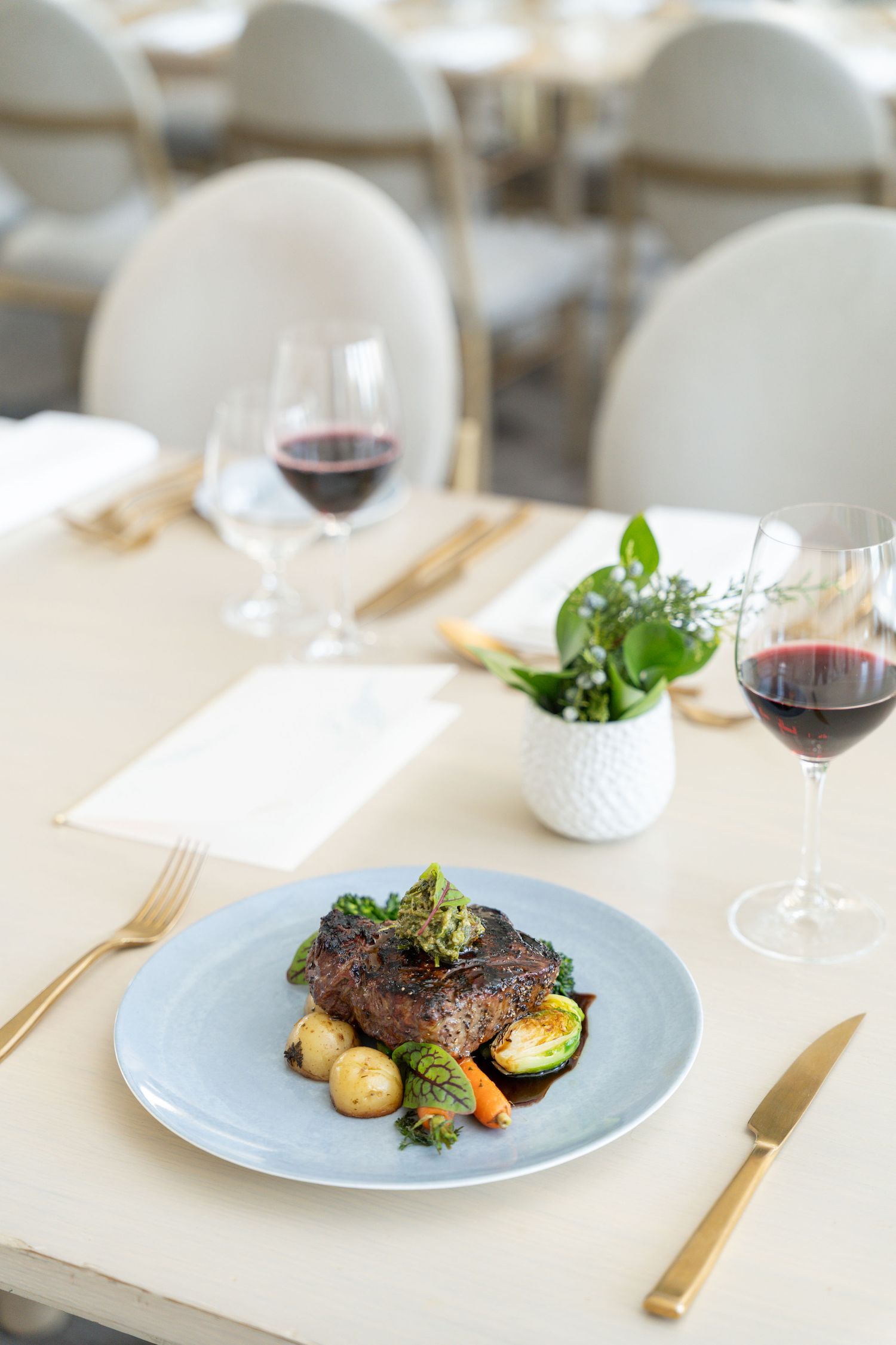 Elegant plated steak dinner with roasted vegetables and red wine served on a light blue plate in an upscale restaurant setting.
