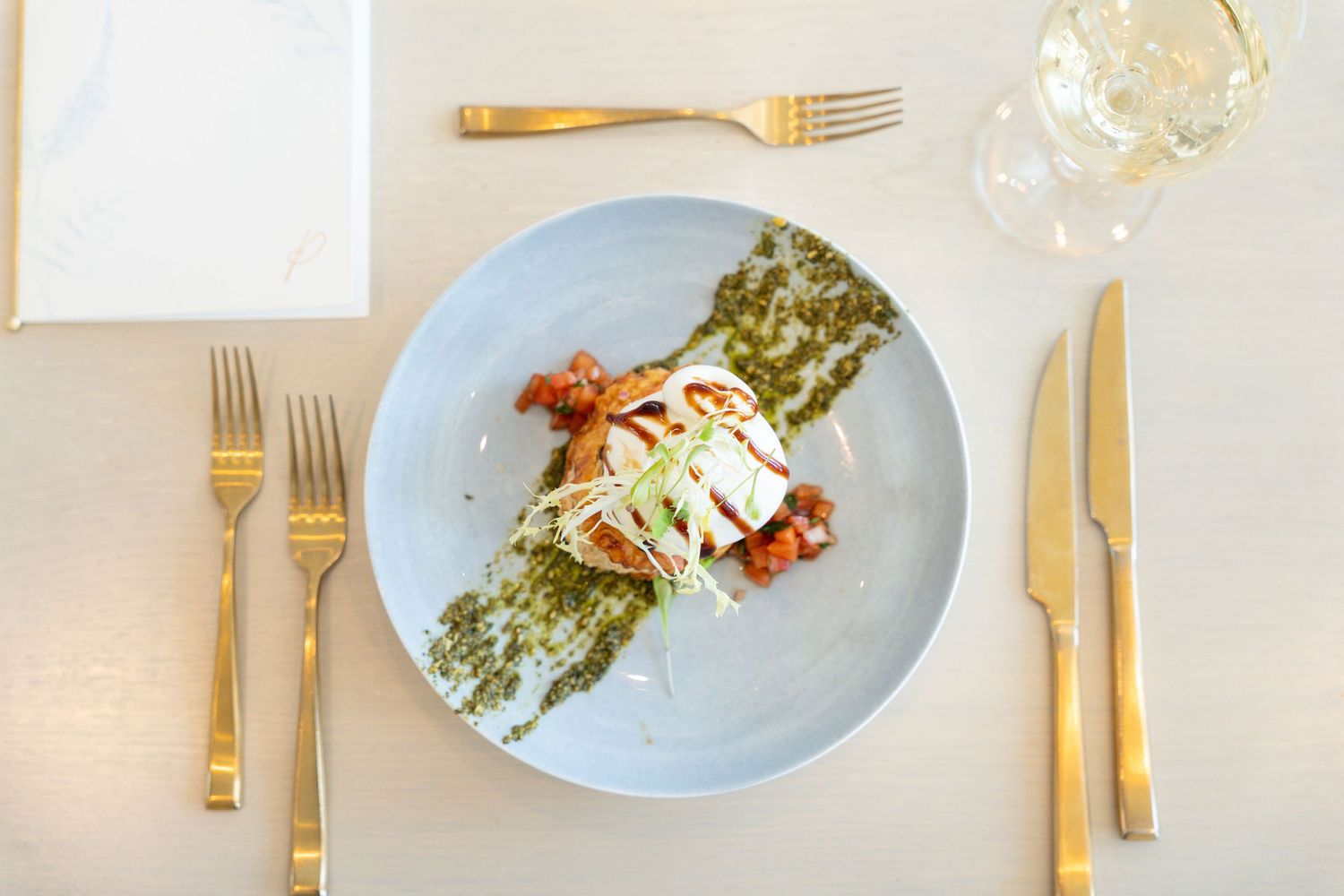Elegant table setting with gold cutlery and white plates showcasing a progression of plated dishes.