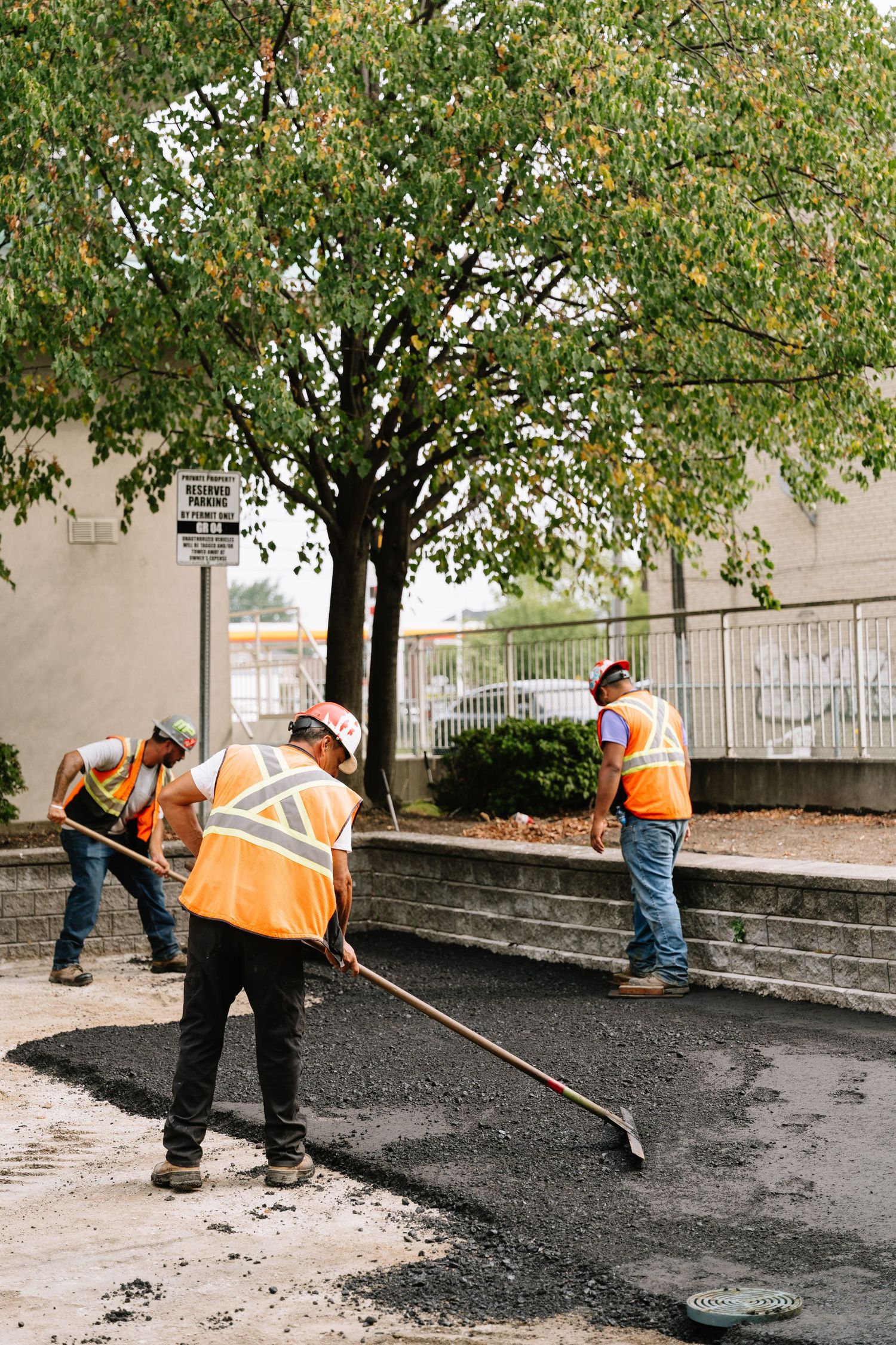 Construction workers in orange safety vests laying asphalt on a curved pathway.