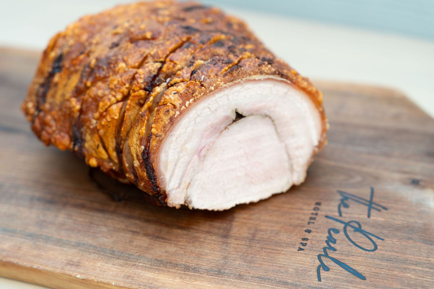 Sliced roasted pork loin with crispy skin displayed on a wooden cutting board.