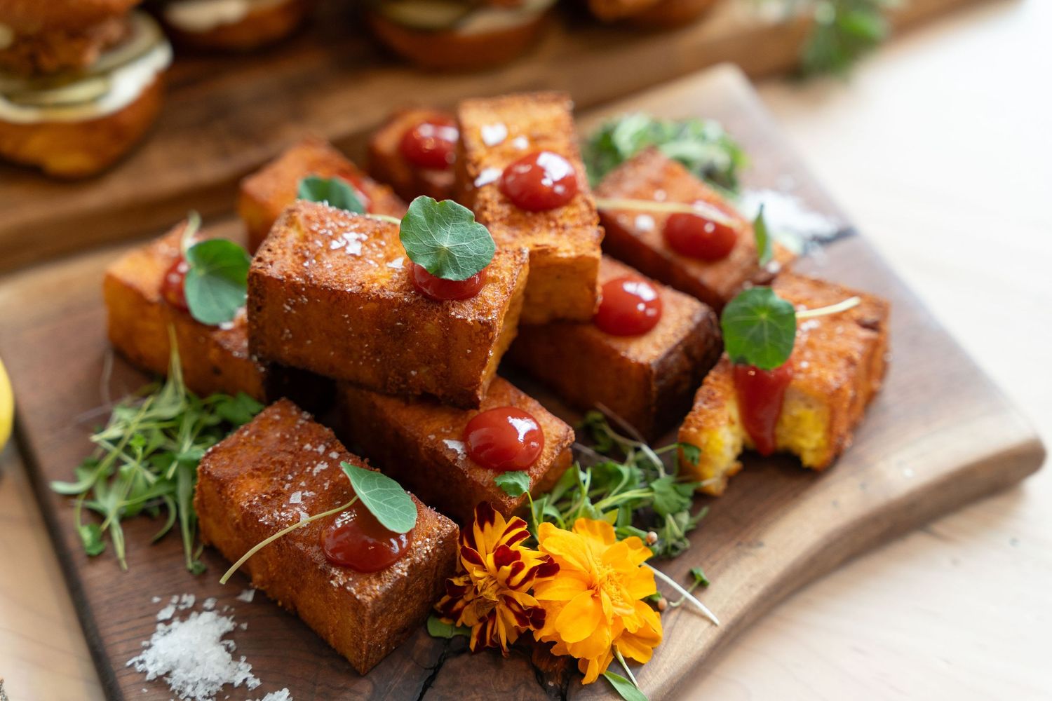 Close-up of gourmet appetizers garnished with orange flowers and fresh herbs on a slate serving board.