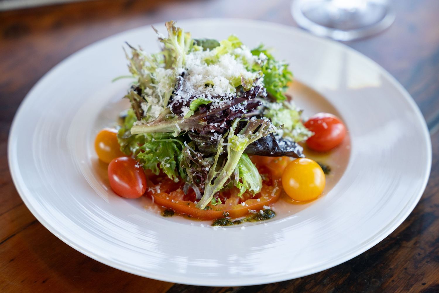 Elegant plated dishes with fresh greens and cherry tomatoes served on white plates at an upscale restaurant.