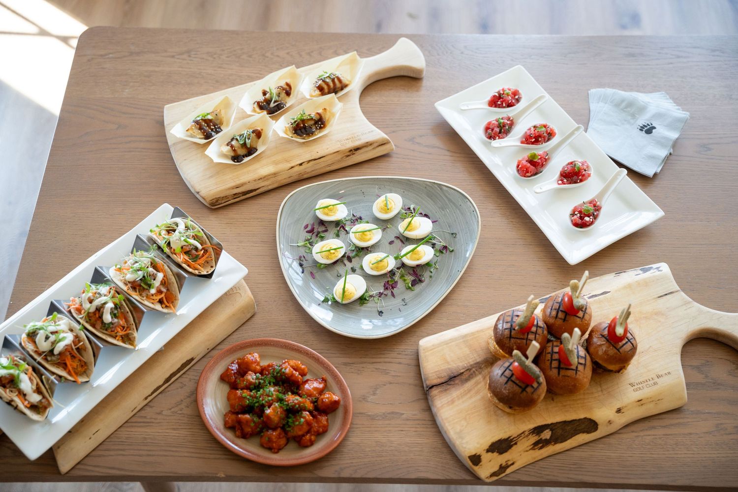 Assorted appetizers and small plates arranged on wooden boards and white plates across a restaurant table setting.