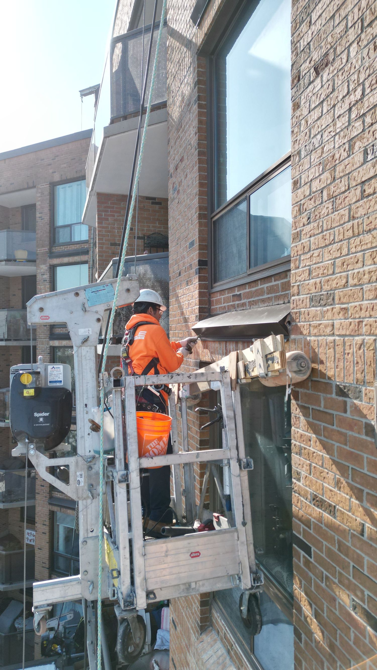 Maintenance workers on elevated lift platforms perform repairs along a brick building facade.