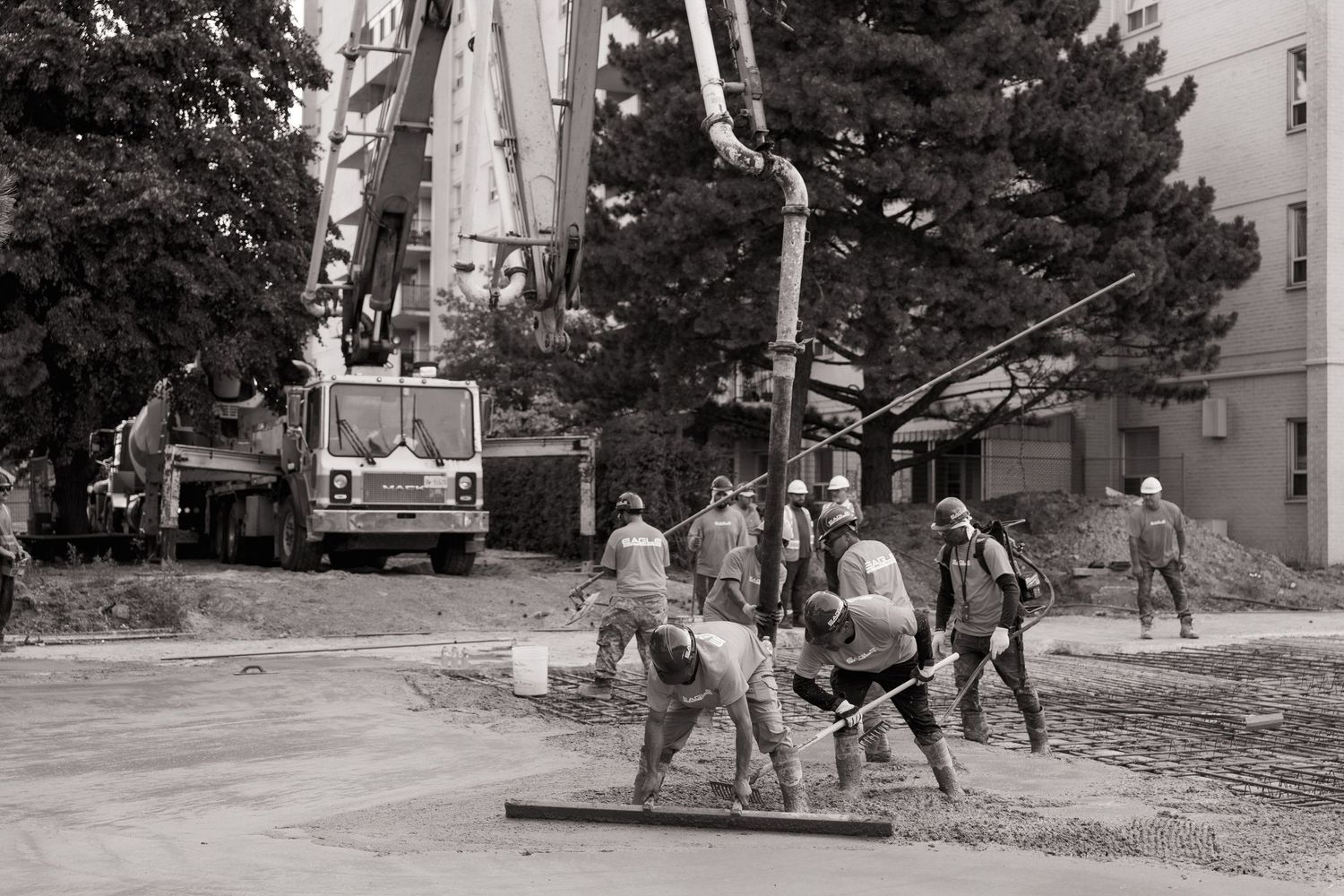 Black and white photo of construction workers leveling concrete near a crane and buildings.