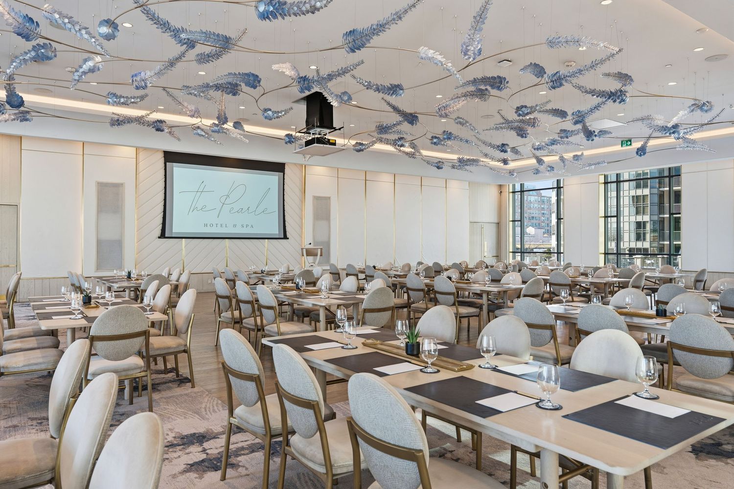 Modern restaurant interior with white chairs and wooden tables arranged in rows under pendant lighting fixtures.