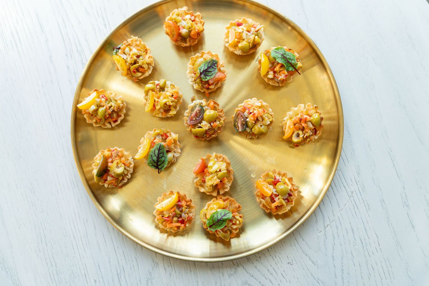 Golden appetizer platter filled with bite-sized crab cakes garnished with fresh herbs.