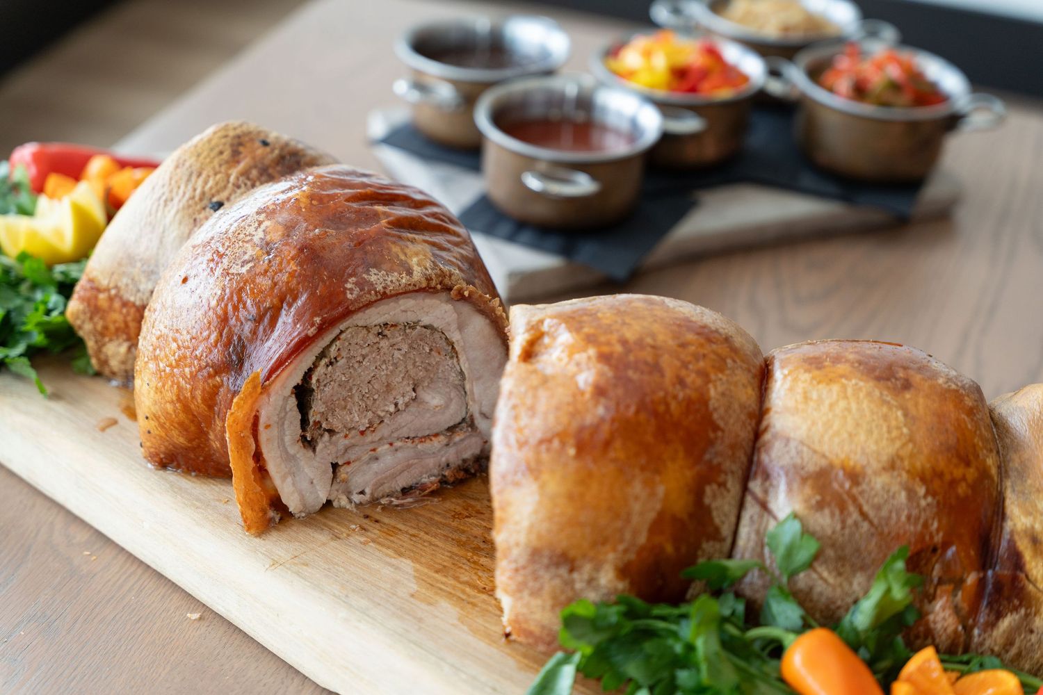 Freshly baked crusty bread rolls arranged in rows on a wooden cutting board with herbs and dipping sauces.