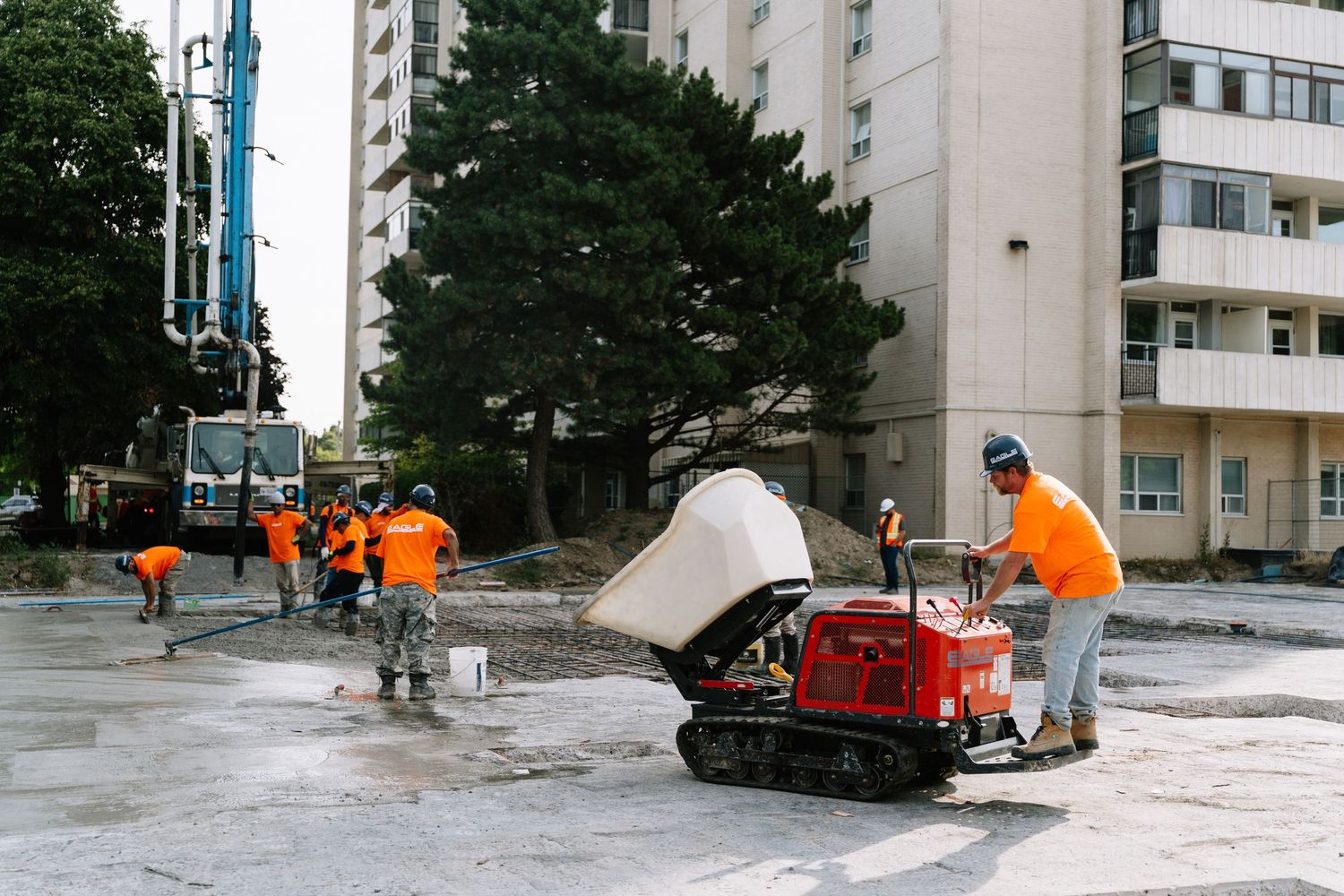 Snow removal crew in bright orange uniforms clearing snow near residential apartment buildings.