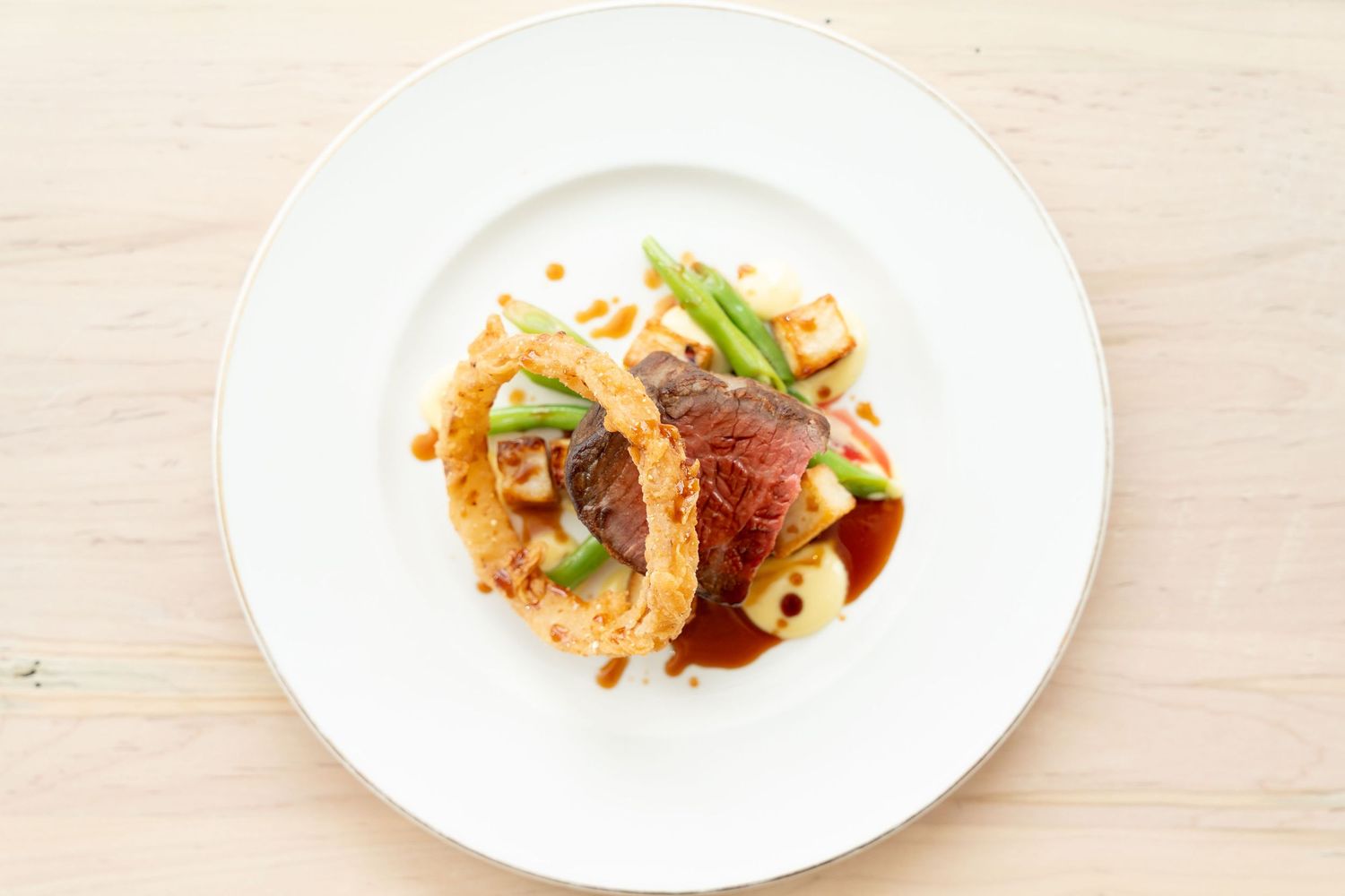 Fine dining plates with artistic food presentation arranged on a light wooden table.