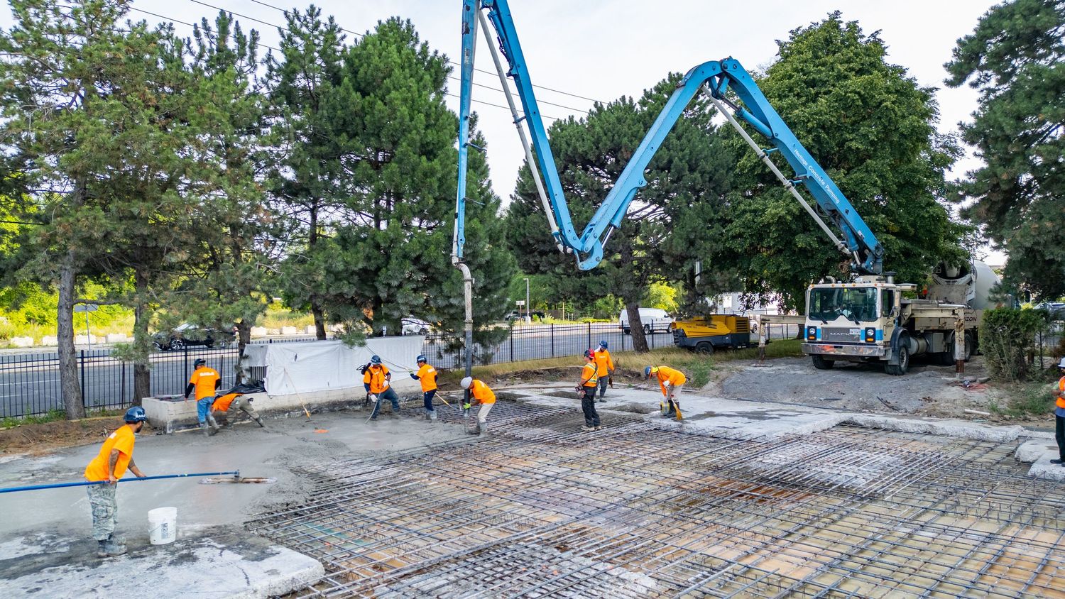 Construction workers prepare steel reinforcement grid for concrete foundation at outdoor building site.