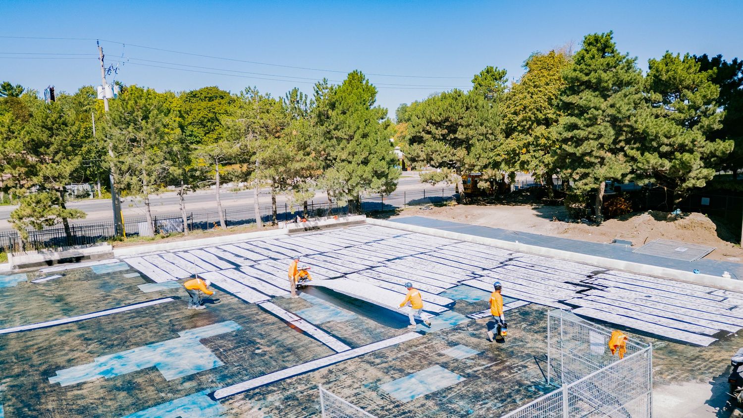 Aerial view of workers clearing snow from an outdoor ice rink surrounded by pine trees.