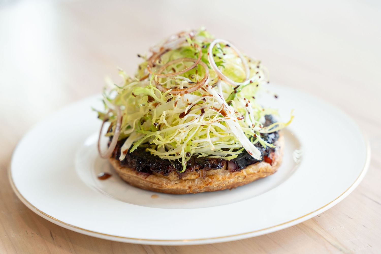 A sandwich on a whole grain bun topped with fresh sprouts and dark ingredients sits on a white plate.