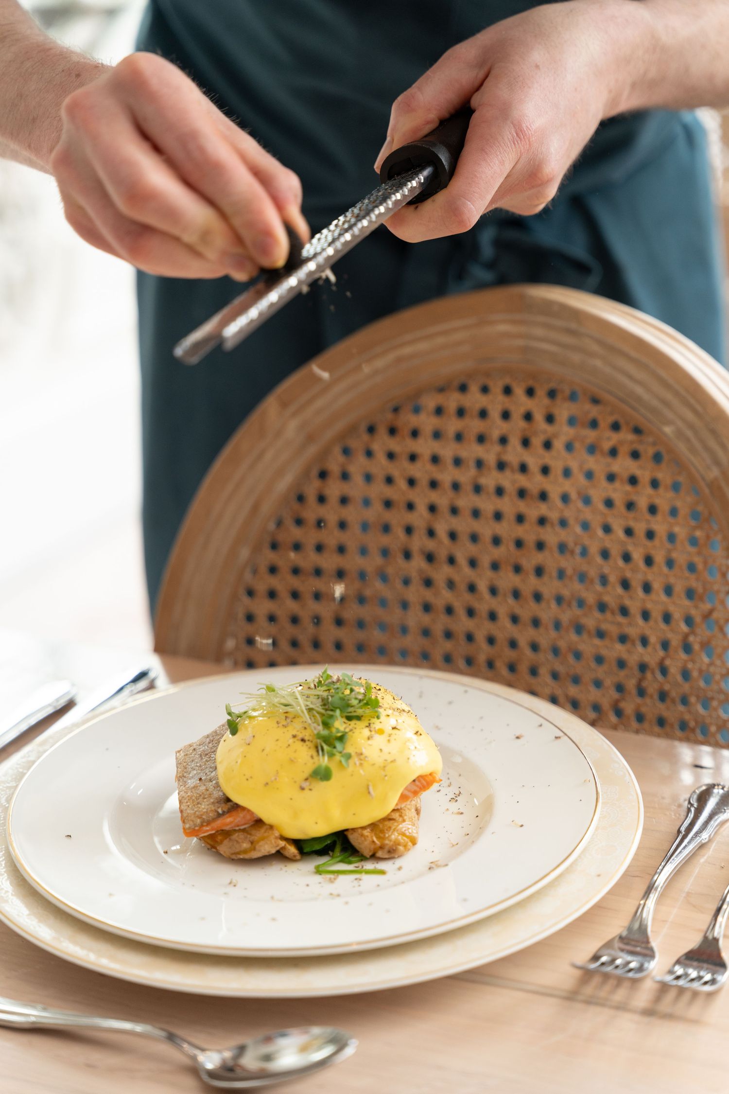 A sequence of hands serving and garnishing an elegant plated dish with yellow sauce and fresh herbs on a white plate.