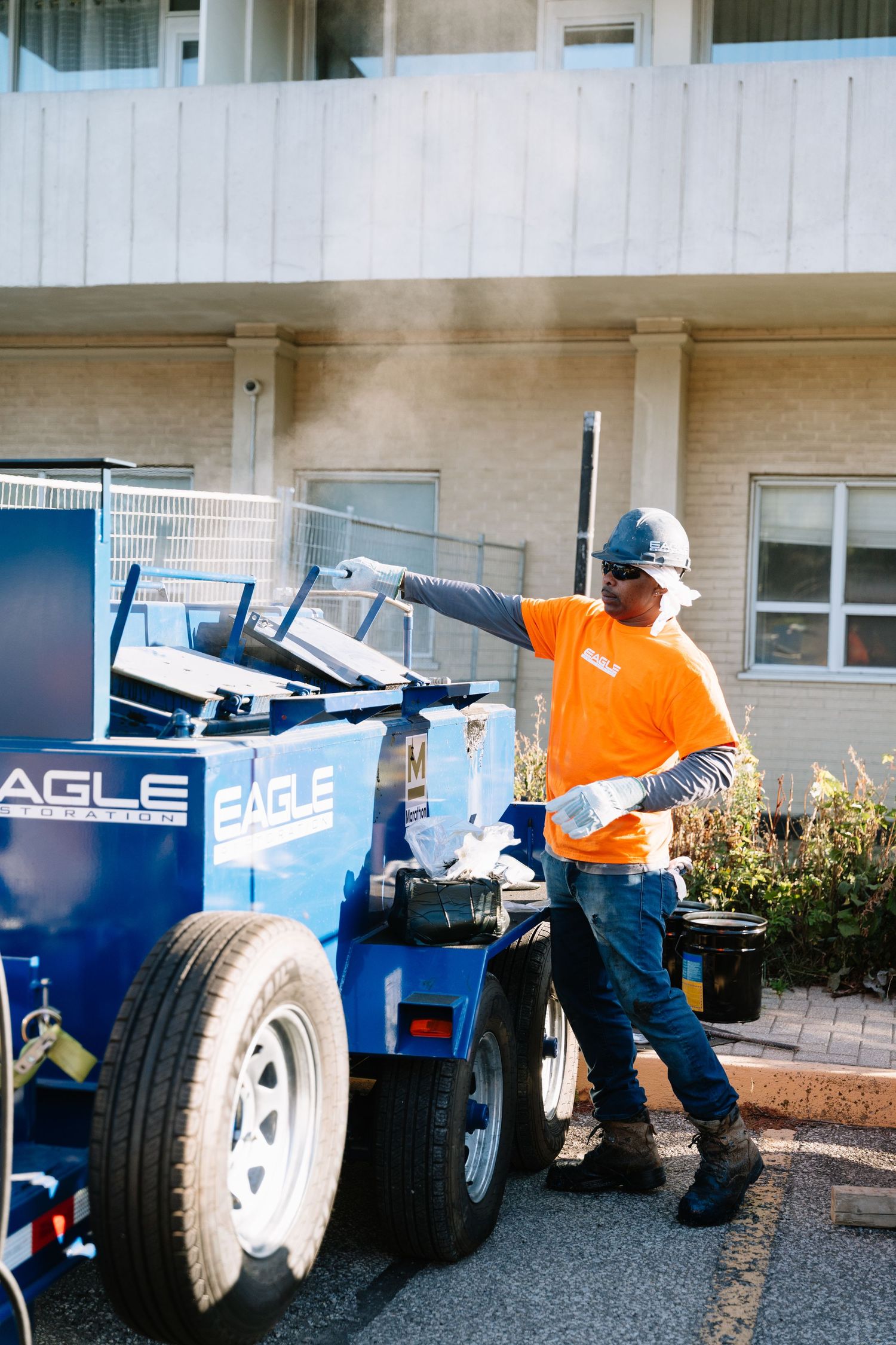 Worker in orange safety vest adjusts equipment on Eagle branded industrial machinery in parking lot.