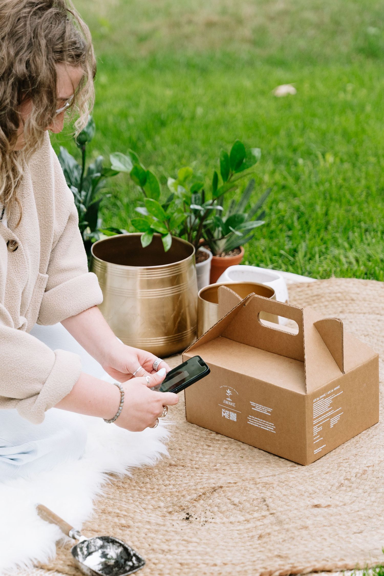 Person sitting on outdoor blanket with cardboard boxes and potted plants arranges items on a sunny day.