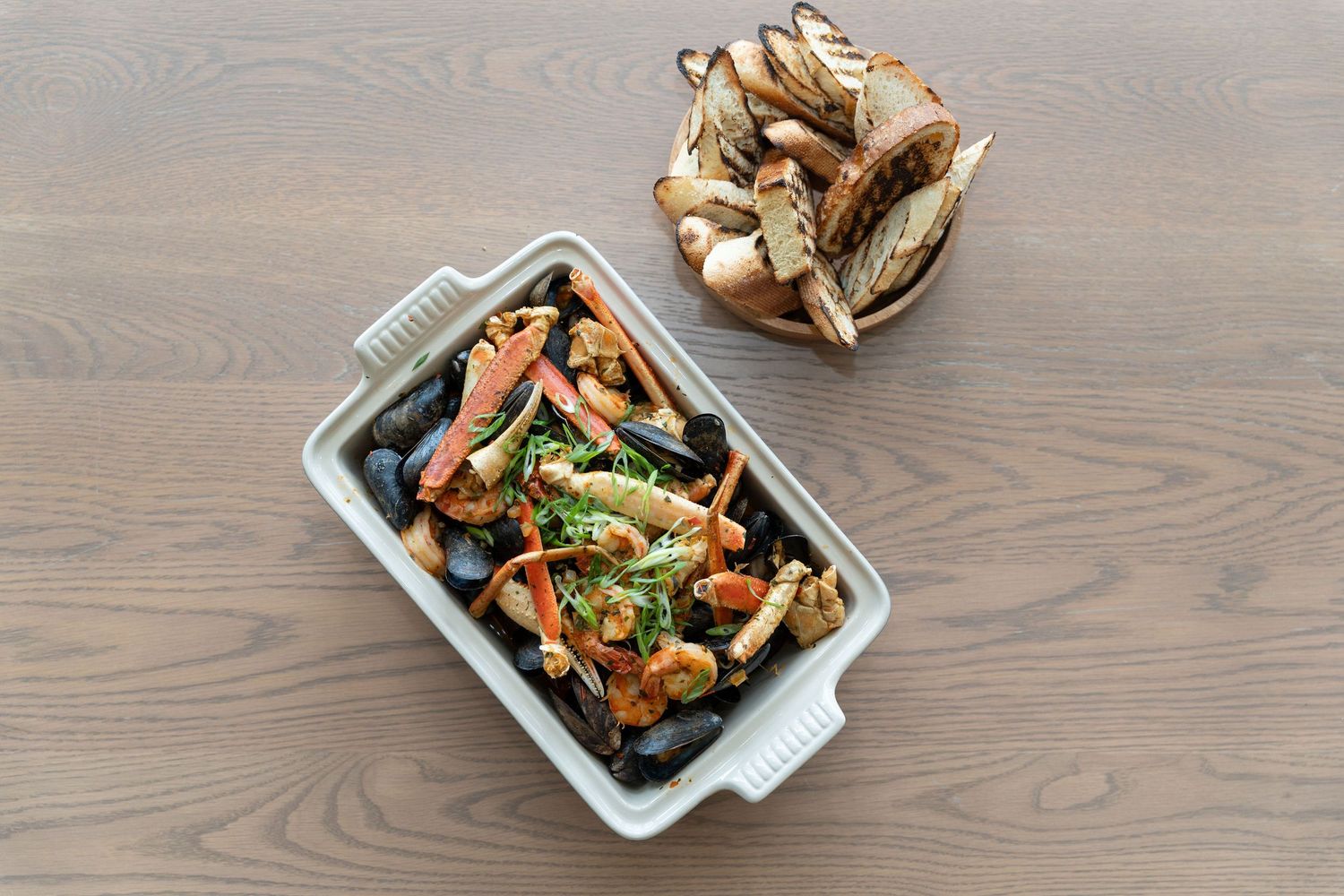 Roasted vegetables and mushrooms served in white ceramic baking dishes on wooden surface.