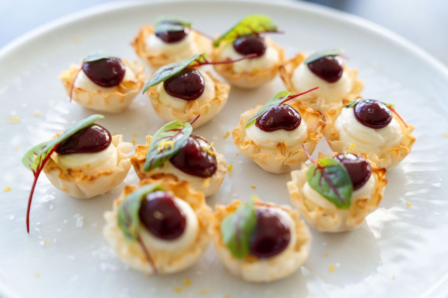 Mini phyllo tart shells filled with cream and topped with cherries and herbs.