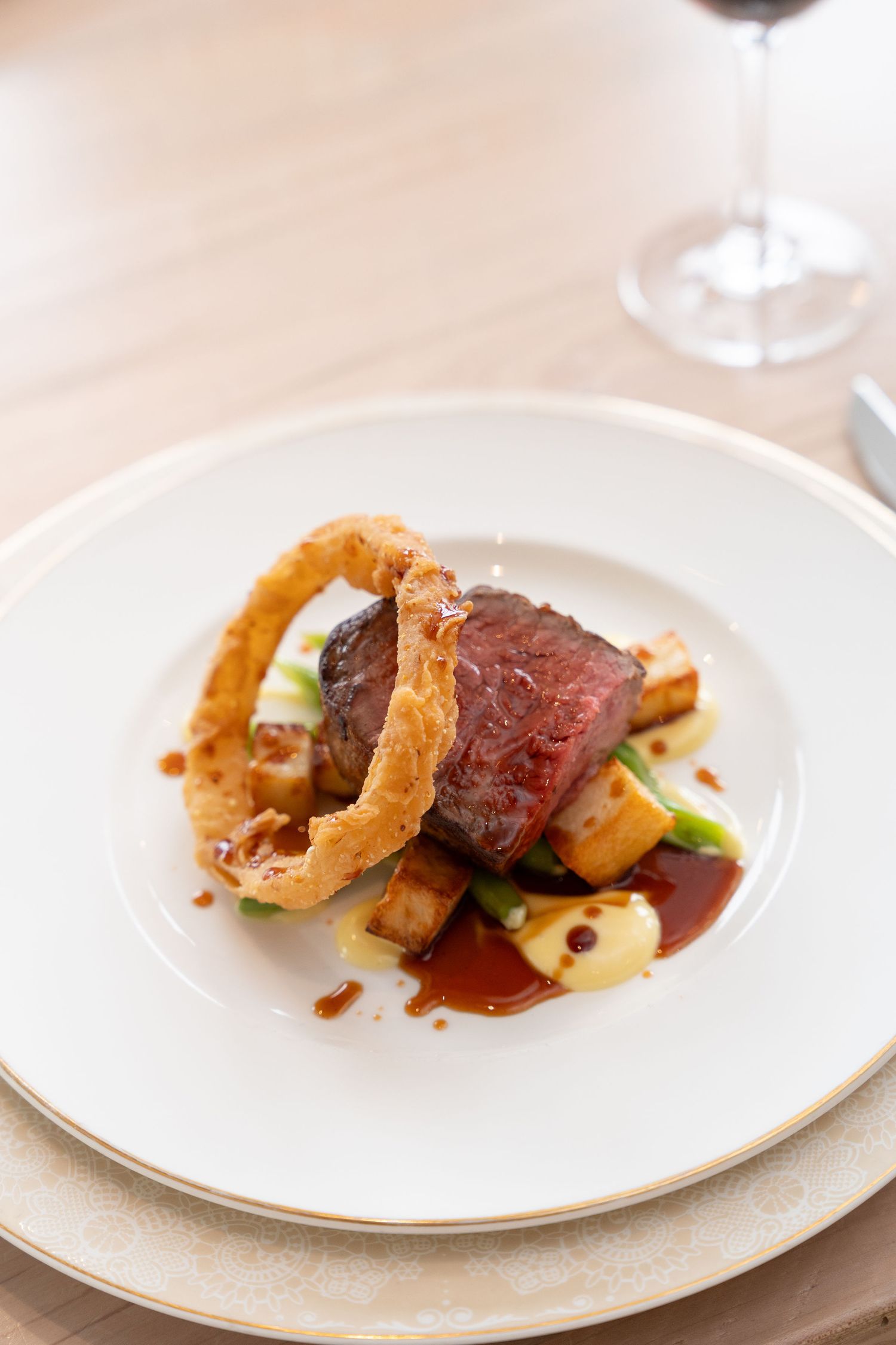 Gourmet beef dish with crispy onion rings and sauce plated elegantly on white china.