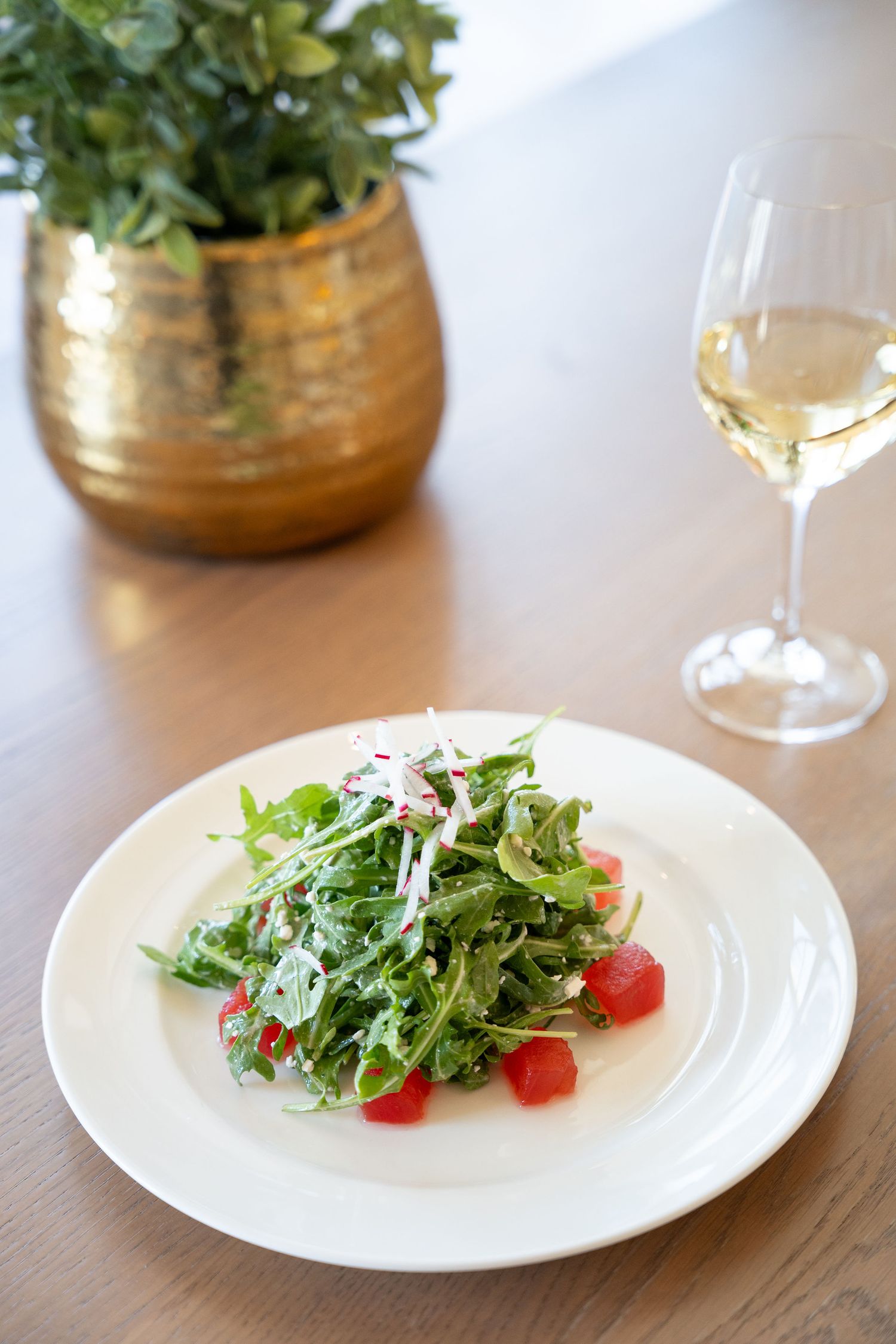 A fresh arugula salad with cherry tomatoes and shaved parmesan cheese served on white plates against a wooden surface.