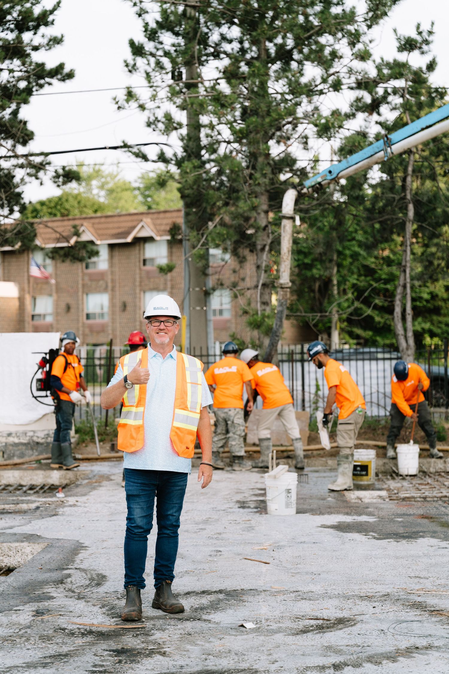 Construction workers in orange safety vests and hard hats work on a concrete site with measuring equipment.
