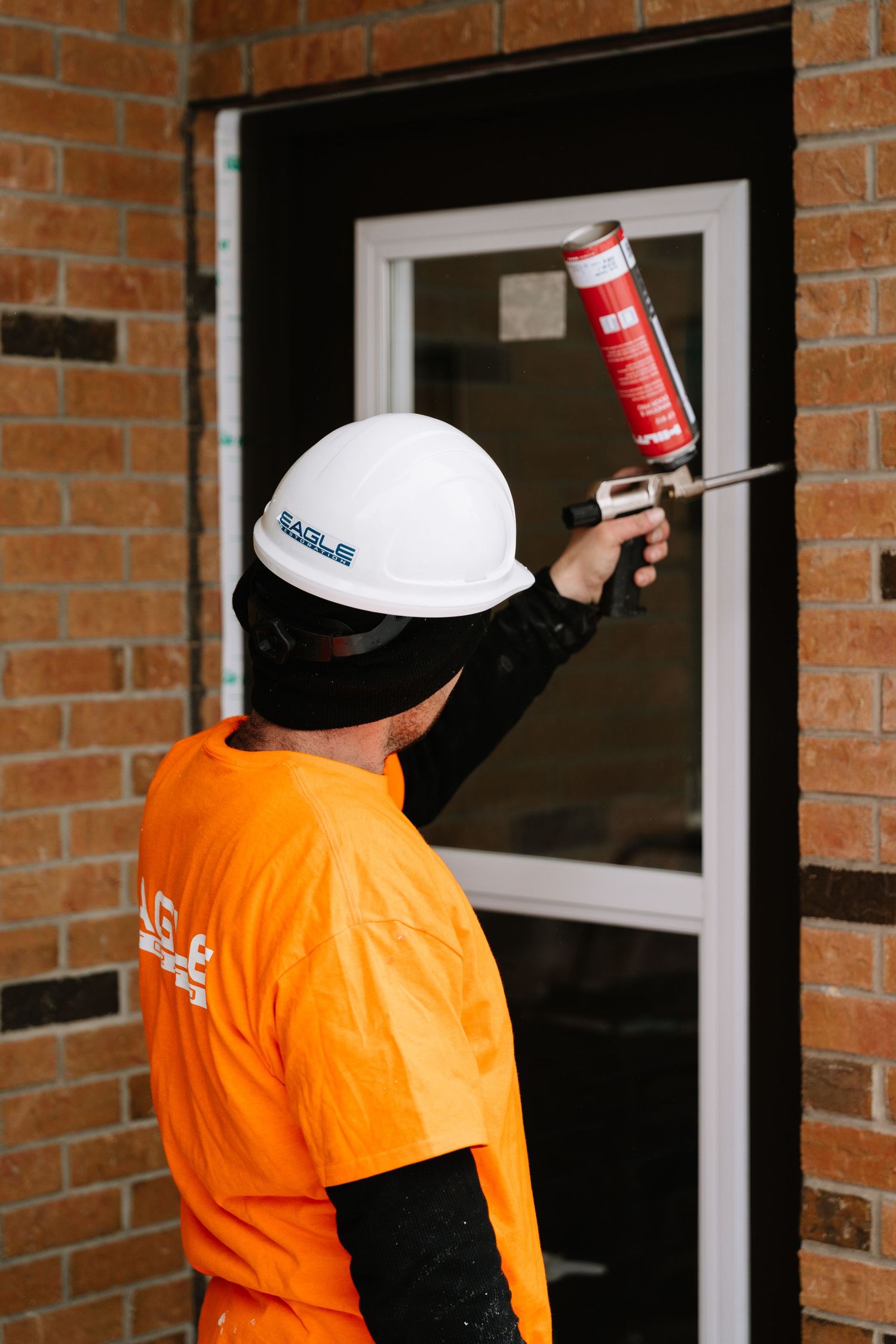 Maintenance crew in orange safety vests work on window installation at brick building exterior.