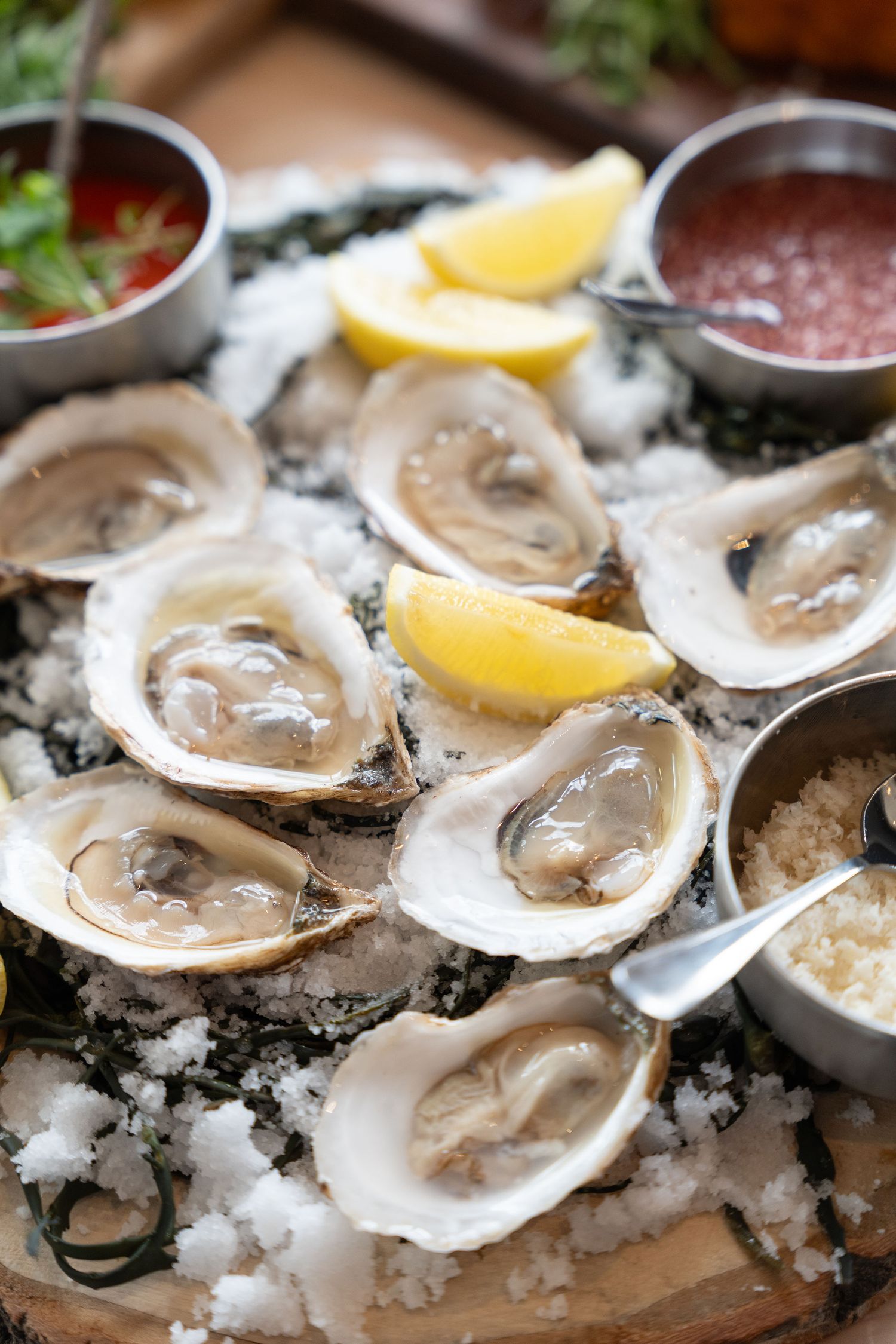 Fresh raw oysters on ice with lemon wedges served on a rustic wooden platter at a seafood restaurant.