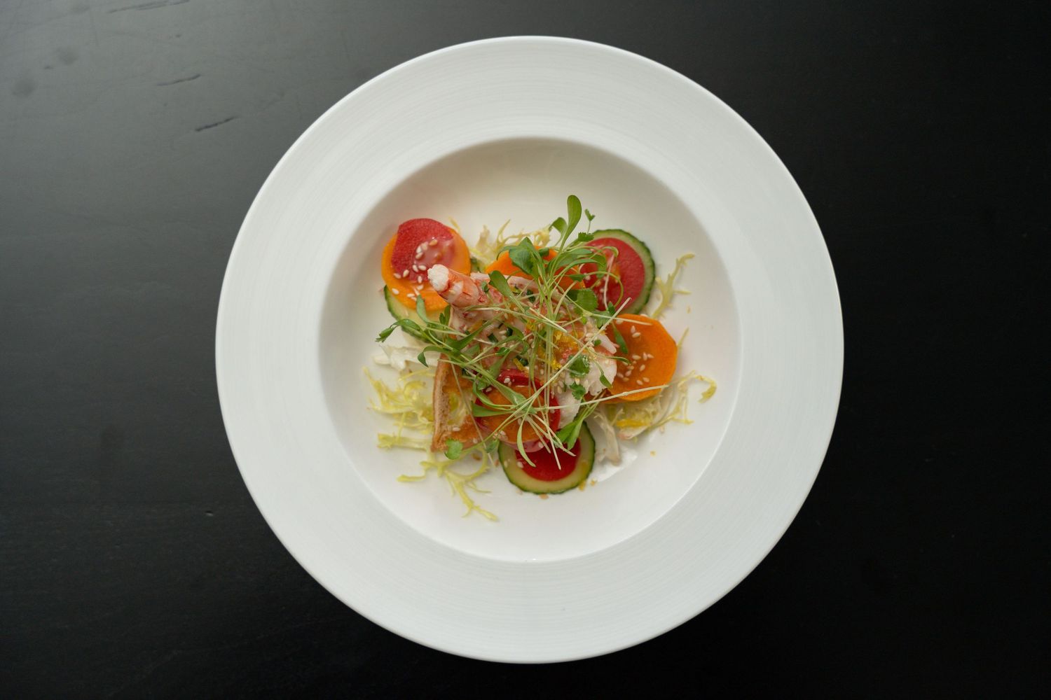 Elegant plated appetizers with microgreens and colorful garnishes served on white dishes against dark background.