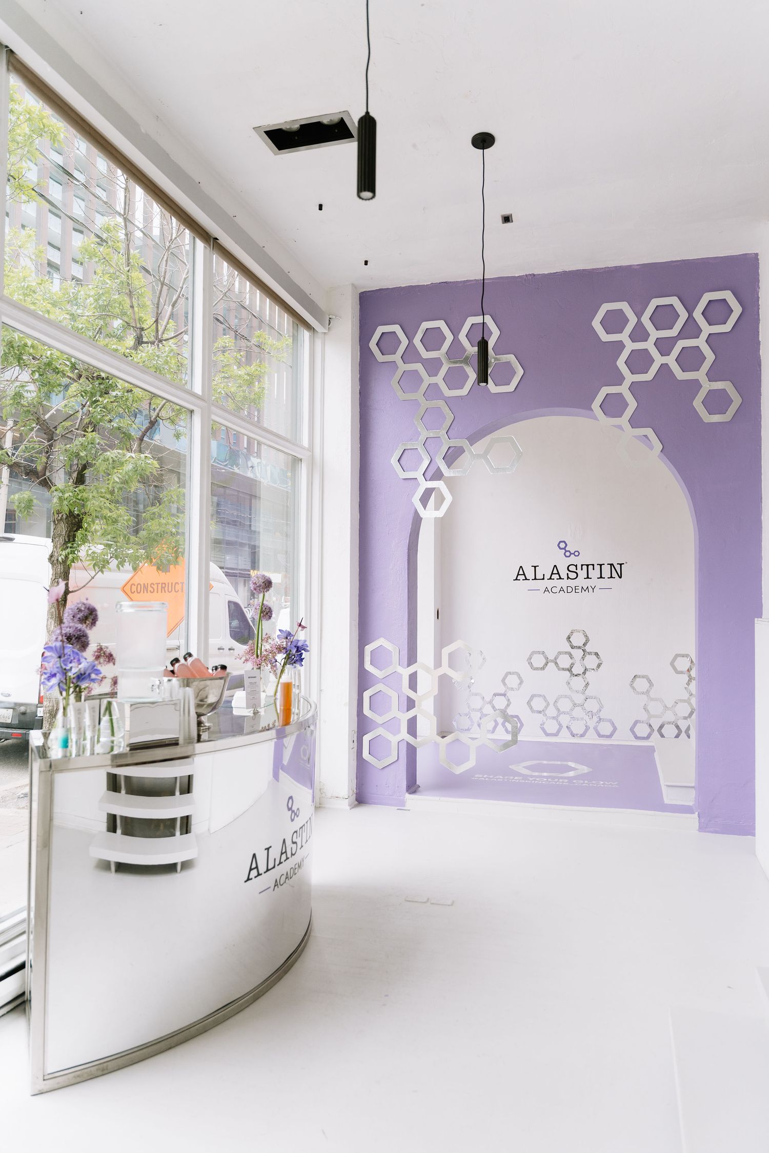 Modern beauty salon interior with purple accent wall, hexagonal wall decor, and white curved reception desk by large windows.