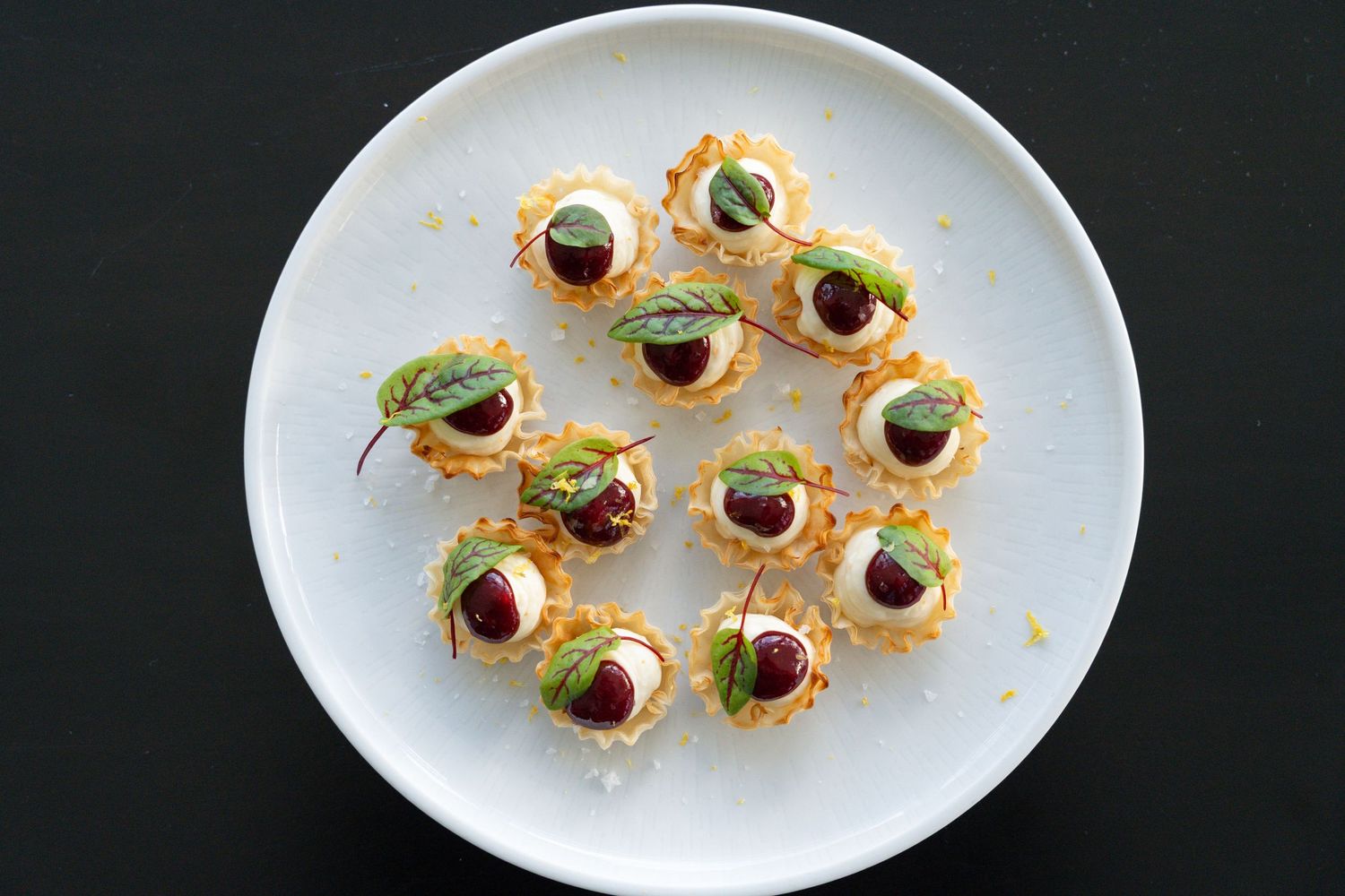 Small round appetizer bites topped with caviar and microgreens arranged on white oval plates.