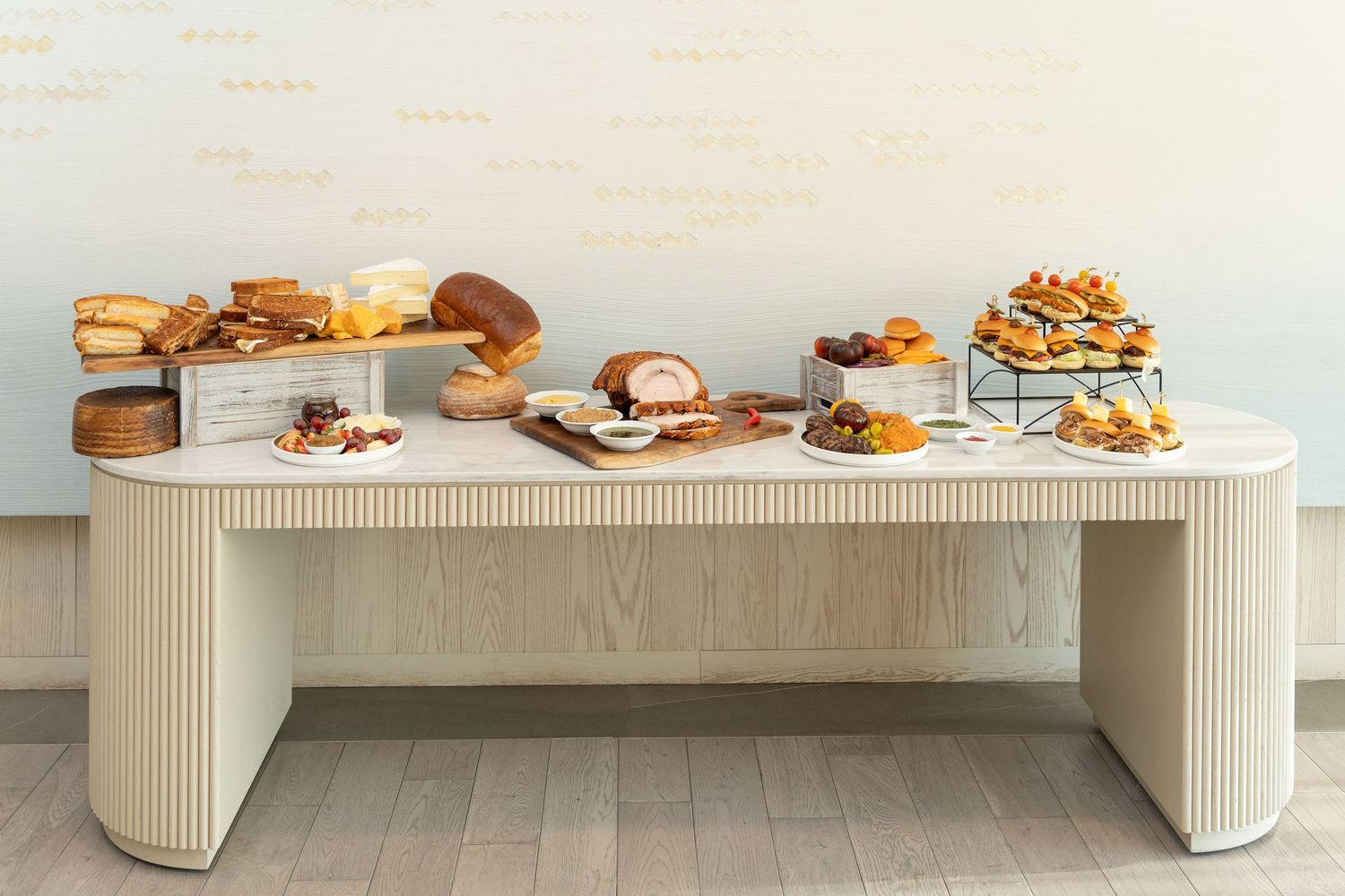 A long white curved display table with various food items and desserts arranged on top against a light colored wall.