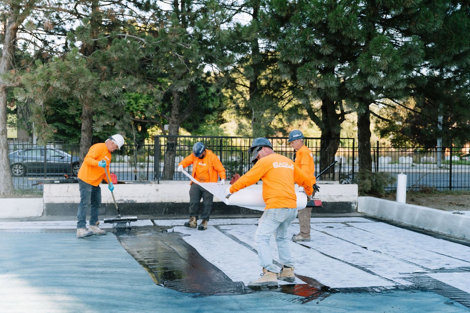 Workers in orange safety vests working together to level a concrete surface at a construction site.