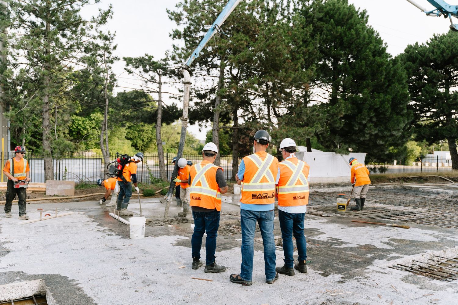 Construction workers in orange safety vests inspect a concrete surface at an outdoor worksite.