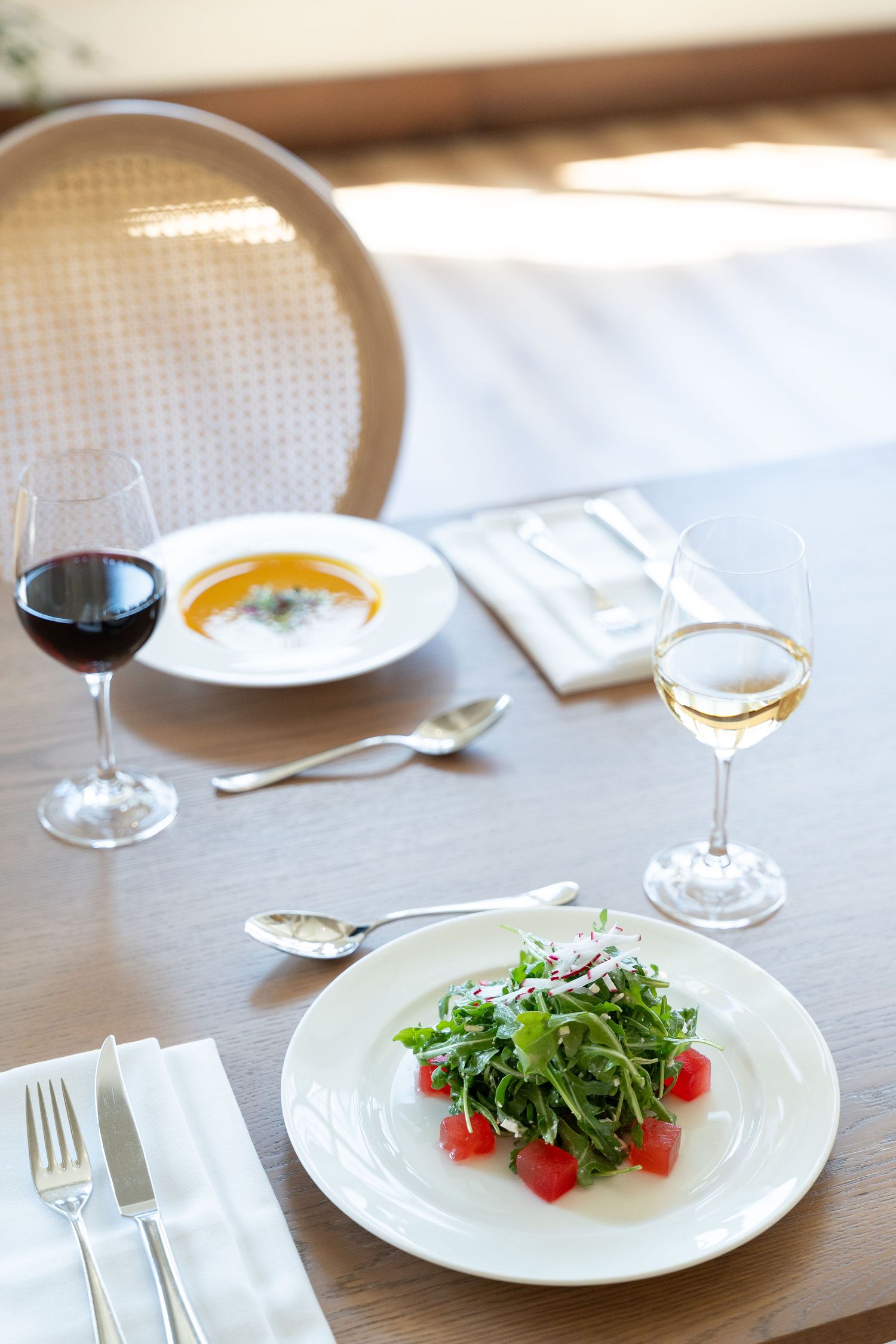 Elegant table setting with wine glasses and fresh green salad plates arranged on a wooden restaurant table.