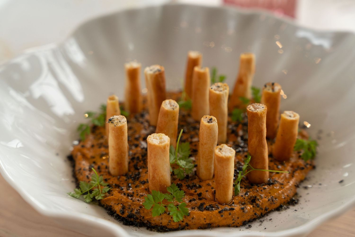Artistic plating of vertical pasta tubes arranged on crumbled dark base in white bowl.