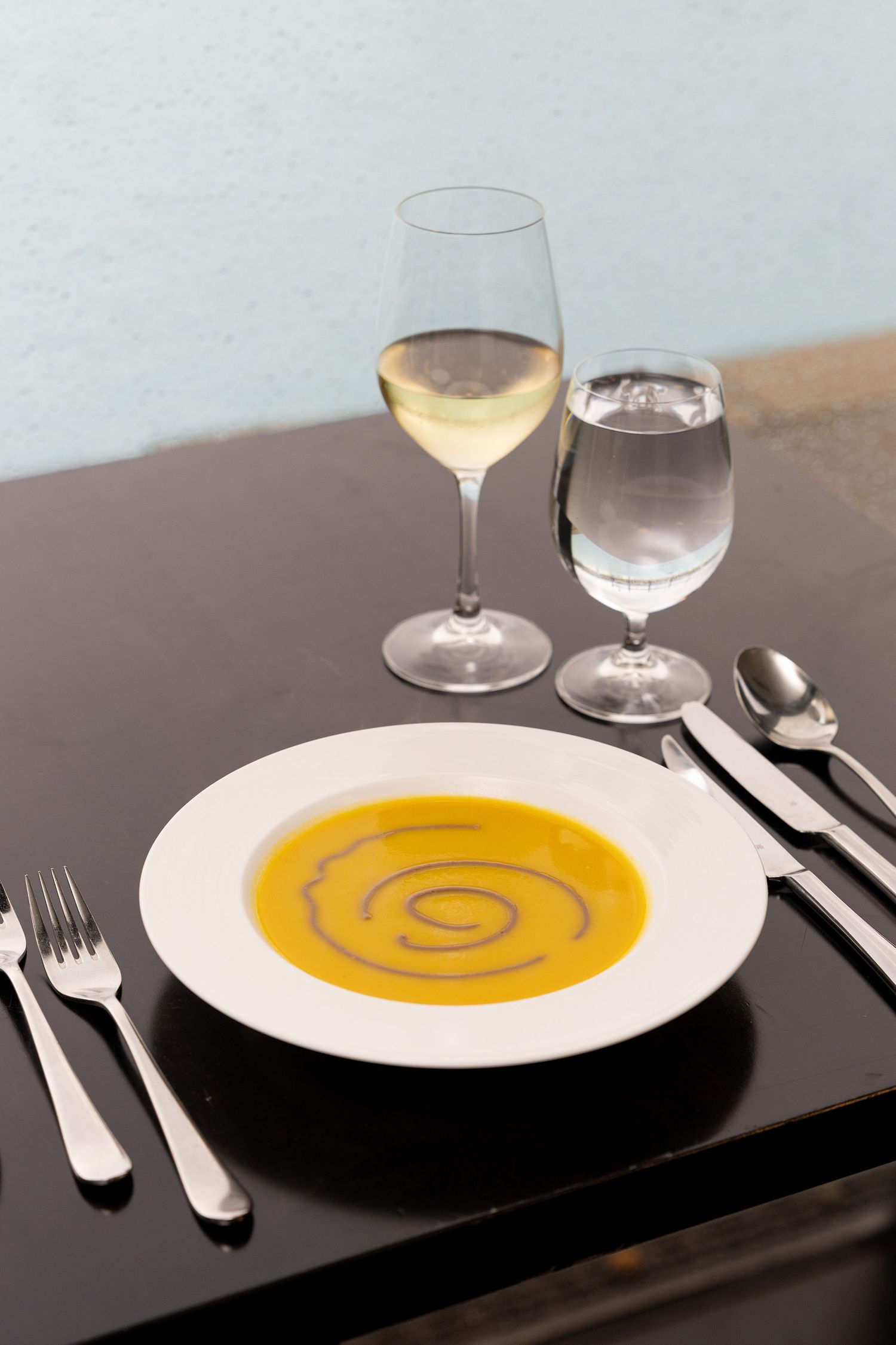 A sequence of four images showing a bowl of creamy orange soup with decorative swirl garnish on a dark table setting.
