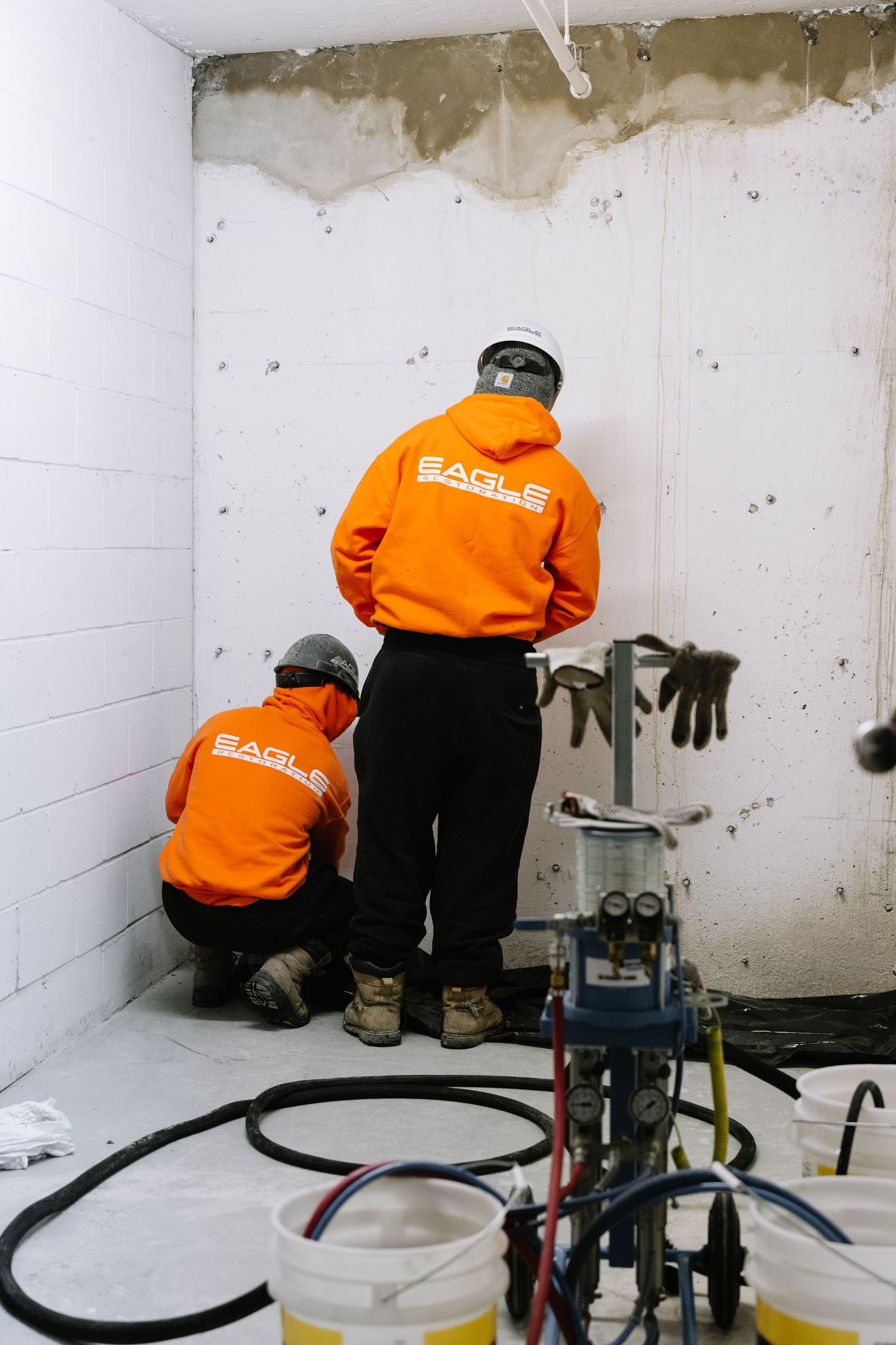 Workers in orange safety gear inspect and repair concrete walls in an industrial setting.