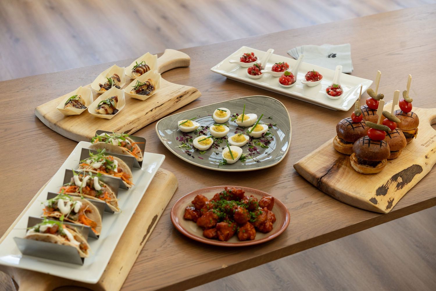 Assorted appetizers and hors d'oeuvres arranged on wooden serving boards and plates at a catering event.