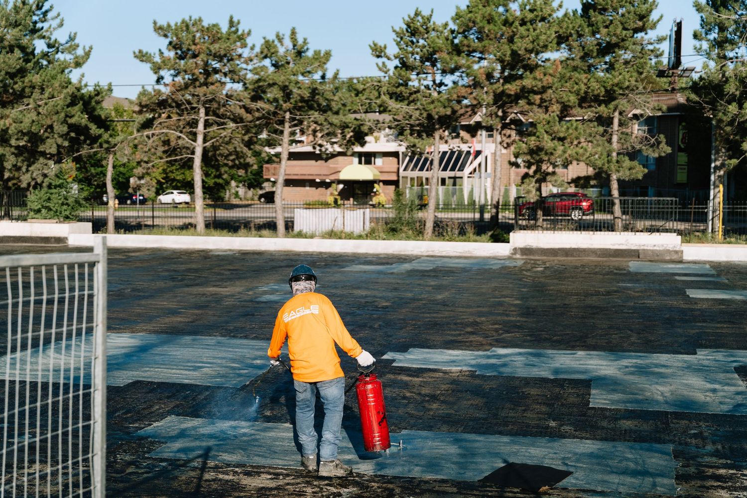 A person in a yellow jacket walks on a frozen outdoor ice rink holding a red bucket near a hockey goal.