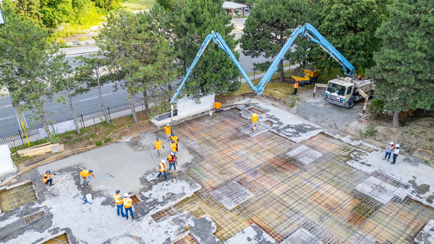 Aerial view of construction workers installing steel rebar grid framework on a concrete foundation at a building site.