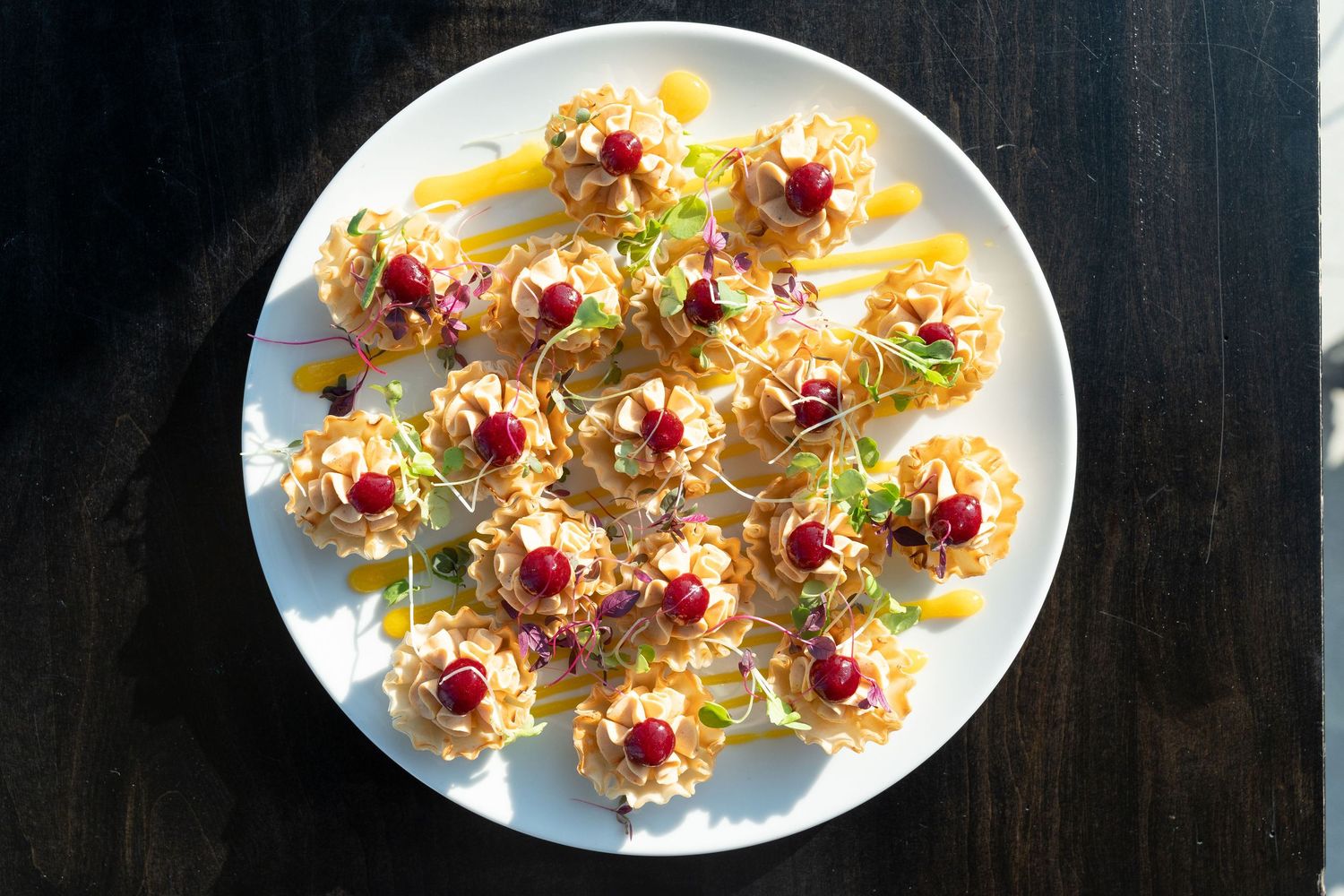 Small appetizer bites with pomegranate seeds and microgreens arranged on white plates against a dark background.