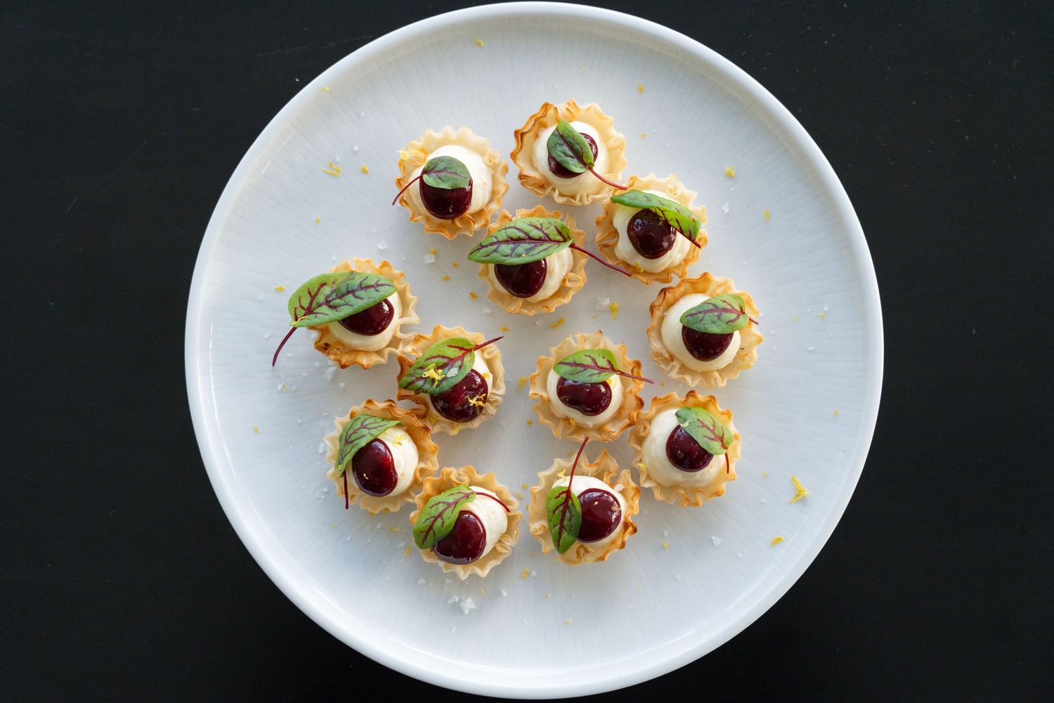 Elegant appetizer bites garnished with black olives and microgreens arranged on white oval plates.