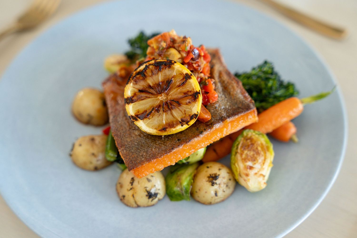 Grilled fish fillet served with roasted vegetables and potatoes on a white plate.